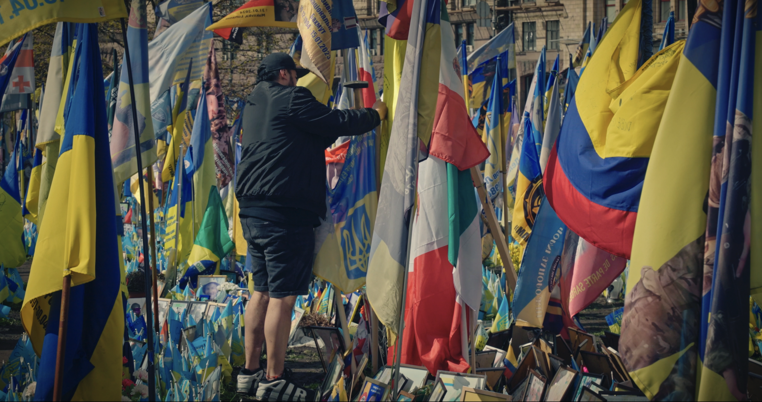 A man adjusts a flag at a Kyiv memorial honoring fallen soldiers from across Ukraine.