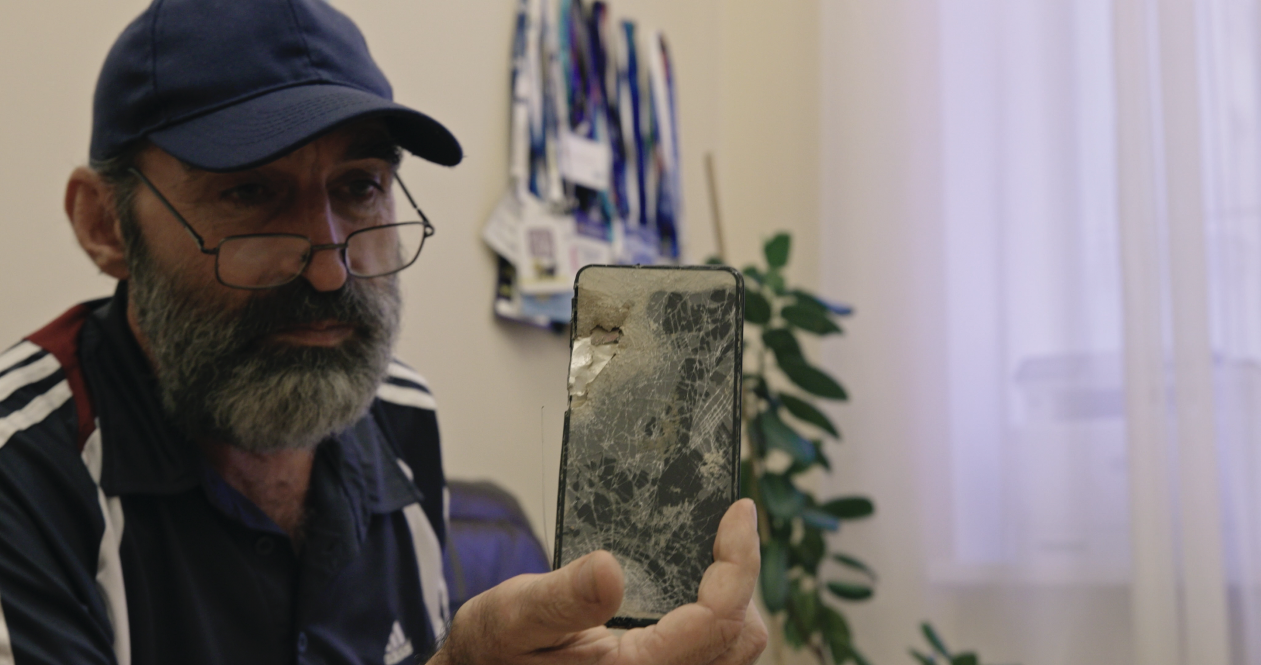 Rustem Bilyalov holds up the shattered phone of his teenage son Emir, who was killed by a Russian missile on the first day of the full-scale invasion. In the documentary, Rustem meets with Eskender Bariiev to discuss how justice can be pursued.